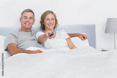 Photo: Relaxed couple watching tv in bed looking at camera Relaxed couple watching tv in bed looking at camera