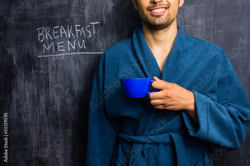 Photo: Man in robe next to breakfast menu on blackboard Man in robe next to breakfast menu on blackboard