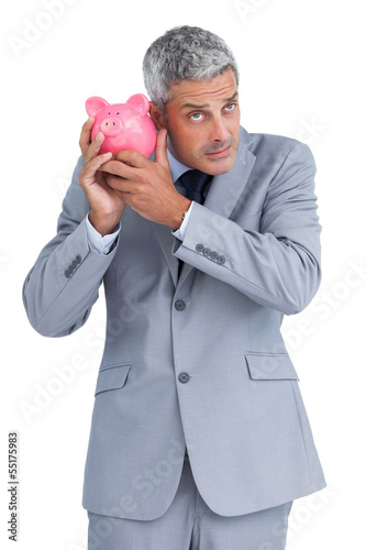 Photo: Doubtful businessman holding piggy bank Doubtful businessman holding piggy bank