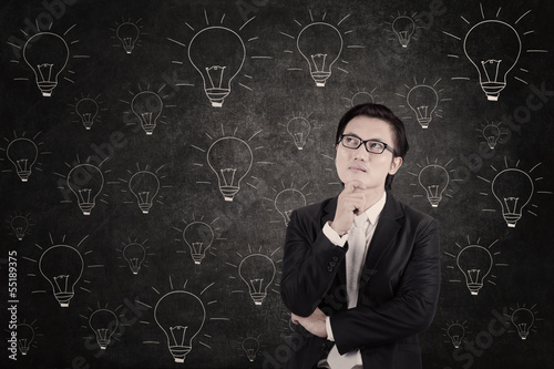 Photo: Asian businessman concentrating on lightbulbs blackboard Asian businessman concentrating on lightbulbs blackboard