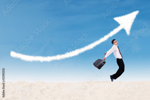 Photo: Businessman jumping under profit arrow sign Businessman jumping under profit arrow sign