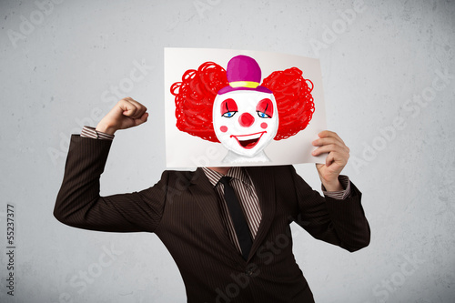 Photo: Businessman holding a cardboard with a clown on it in front of h Businessman holding a cardboard with a clown on it in front of h