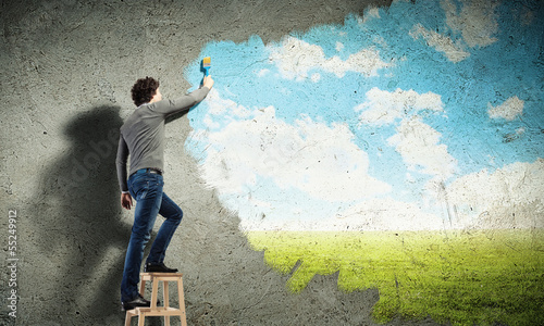 Photo: Young man drawing a cloudy blue sky Young man drawing a cloudy blue sky