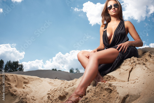 Photo: Beautiful girl wearing black dress sitting on the sand Beautiful girl wearing black dress sitting on the sand