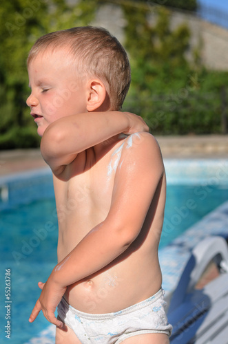 Photo: Small boy in a swimsuit applying sunscreen Small boy in a swimsuit applying sunscreen