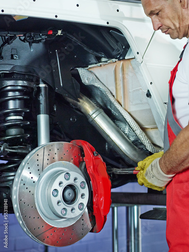 Photo: Car mechanic in a garage repairs a bracke Car mechanic in a garage repairs a bracke