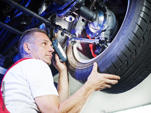 Photo: Mechanic in a garage checks a tyre of a car Mechanic in a garage checks a tyre of a car