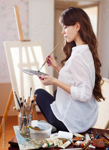 Photo: female artist near easel with blank canvas female artist near easel with blank canvas