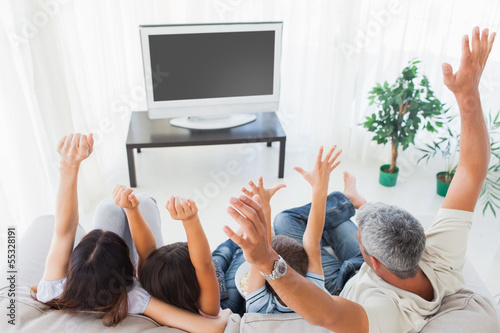 Photo: Family raising their arms in front of television Family raising their arms in front of television