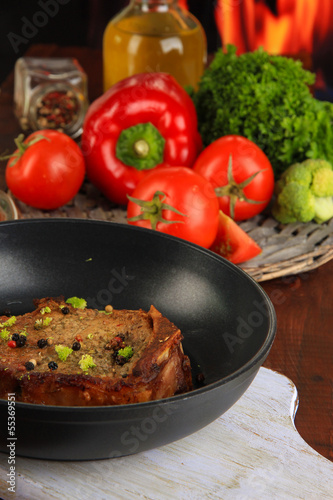 Photo: Piece of fried meat on pan on wooden table on fire background Piece of fried meat on pan on wooden table on fire background