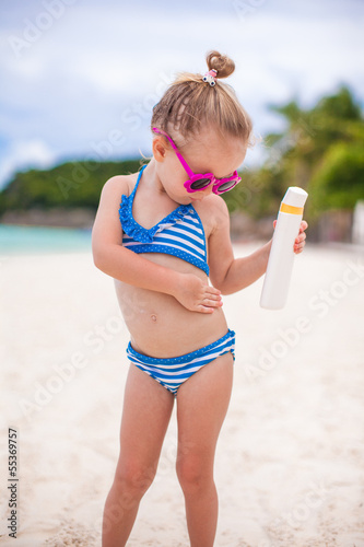Photo: Little adorable girl in swimsuit rubs sunscreen herself Little adorable girl in swimsuit rubs sunscreen herself