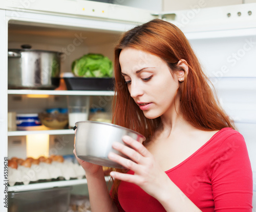 Photo: woman looking for something in pan near fridge woman looking for something in pan near fridge