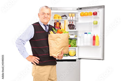 Photo: Mature gentleman holding a paper bag in front of fridge Mature gentleman holding a paper bag in front of fridge