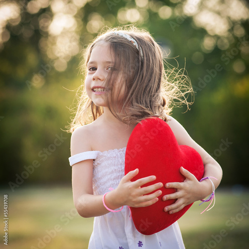 Photo: Sweet girl with red heart outdoors in the park. Sweet girl with red heart outdoors in the park.