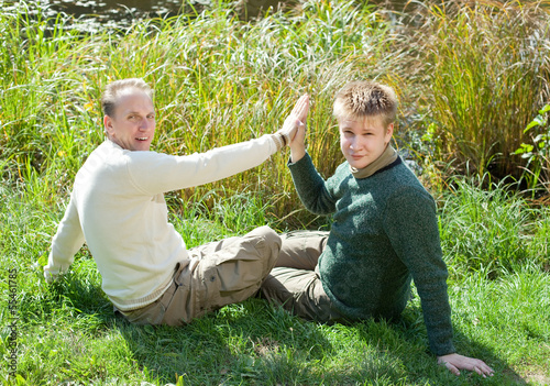 Photo: The father with the son sit on the grassy coast of the lake.. The father with the son sit on the grassy coast of the lake..