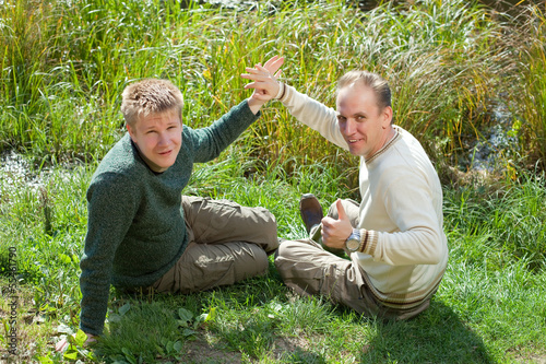 Photo: The father with the son sit on the grassy coast of the lake.. The father with the son sit on the grassy coast of the lake..