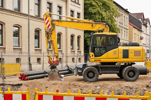 Photo: Ein gelber Bagger vor einem älteren Haus beim Strassenbau Ein gelber Bagger vor einem älteren Haus beim Strassenbau