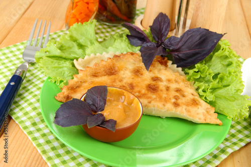 Photo: Tasty chebureks with fresh herbs on plate,on wooden background Tasty chebureks with fresh herbs on plate,on wooden background
