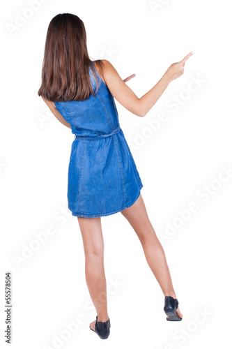Photo: Back view of young brunette woman pointing at wall. cheerful gir Back view of young brunette woman pointing at wall. cheerful gir