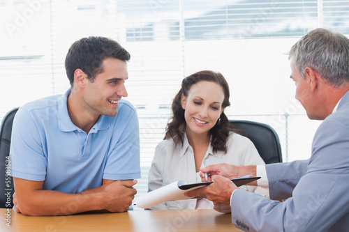 Photo: Smiling couple signing contract with real estate agent Smiling couple signing contract with real estate agent