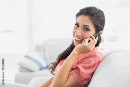 Photo: Content brunette sitting on her sofa on the phone looking at cam Content brunette sitting on her sofa on the phone looking at cam