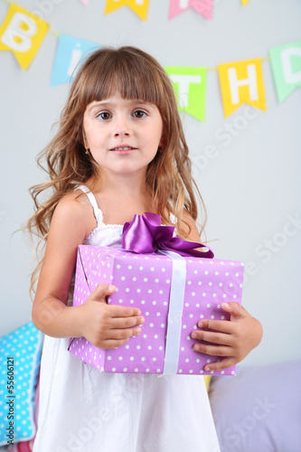 Photo: Little girl with gift in room on grey wall background Little girl with gift in room on grey wall background