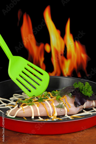 Photo: Raw chicken fillets on dripping pan, on fire background Raw chicken fillets on dripping pan, on fire background