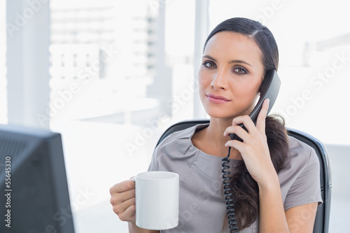 Photo: Serious secretary answering phone and drinking coffee Serious secretary answering phone and drinking coffee