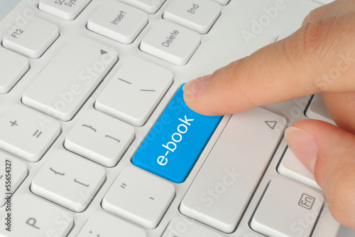 Photo: Hand pushing blue e-book button on white keyboard. Hand pushing blue e-book button on white keyboard.