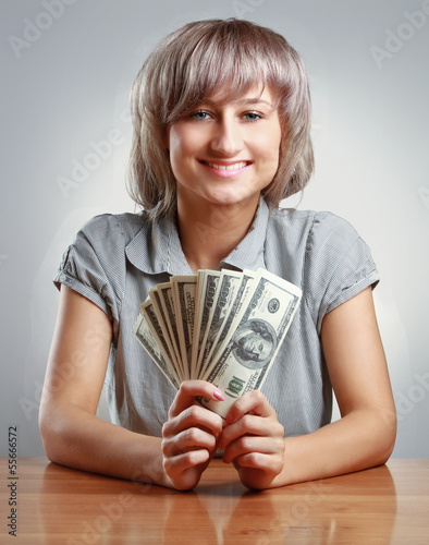 Photo: A young woman sitting on the desk and holding dollars A young woman sitting on the desk and holding dollars