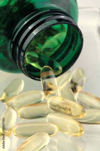 Photo: Fish oil capsules falling out of a green bottle Fish oil capsules falling out of a green bottle