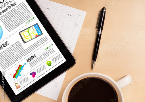 Photo: Tablet pc shows news on screen with a cup of coffee on a desk Tablet pc shows news on screen with a cup of coffee on a desk