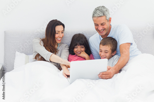 Photo: Smiling family lying in bed using their laptop Smiling family lying in bed using their laptop