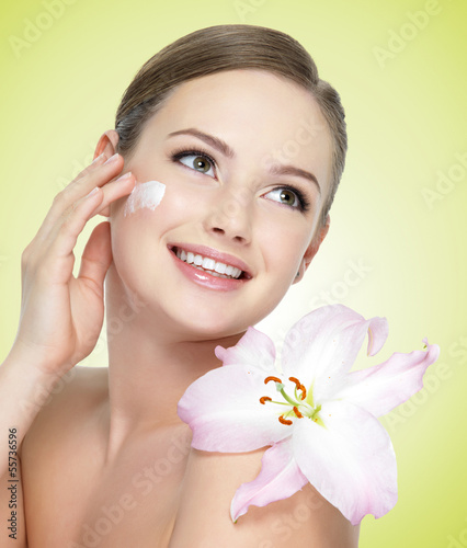 Photo: smiling woman with flower applying cosmetic cream on face smiling woman with flower applying cosmetic cream on face