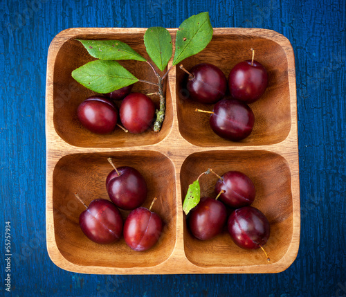 Photo: Plums in a wooden bowl on a blue wooden background Plums in a wooden bowl on a blue wooden background