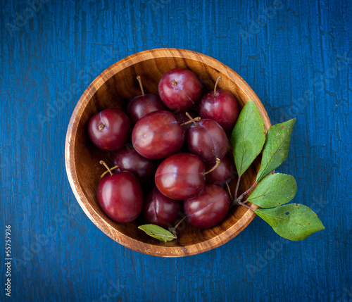 Photo: Ripe plums in a wooden bowl on a blue wooden background Ripe plums in a wooden bowl on a blue wooden background