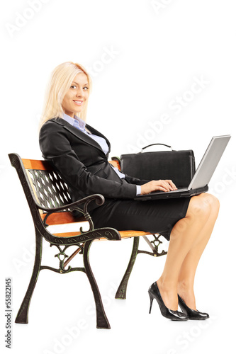 Photo: Smiling businesswoman sitting on a bench and working on a laptop Smiling businesswoman sitting on a bench and working on a laptop