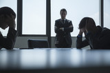 Photo: Three frustrated and overworked business people in the board room with arms crossed and head in hands. Three frustrated and overworked business people in the board room with arms crossed and head in hands.