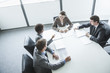 Photo: Four business people sitting around a table and having a business meeting, high angle view Four business people sitting around a table and having a business meeting, high angle view