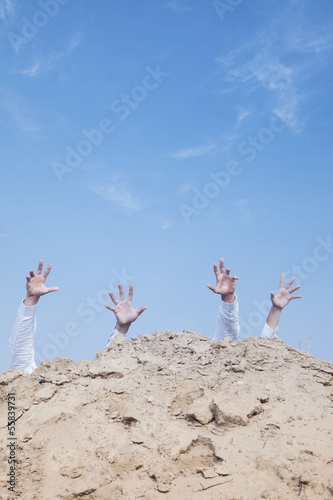 Photo: Close-up of hands of businessmen behind a hill in the desert, reaching upwards Close-up of hands of businessmen behind a hill in the desert, reaching upwards