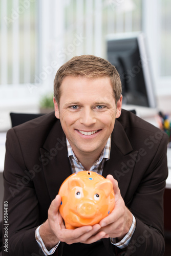 Photo: lächelnder mann im büro mit sparschwein lächelnder mann im büro mit sparschwein