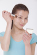 Photo: Young beautiful woman looking into a mirror and applying make up with a make up brush, studio shot Young beautiful woman looking into a mirror and applying make up with a make up brush, studio shot