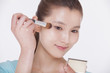 Photo: Young beautiful woman looking into a mirror and applying make up with a make up brush, studio shot Young beautiful woman looking into a mirror and applying make up with a make up brush, studio shot