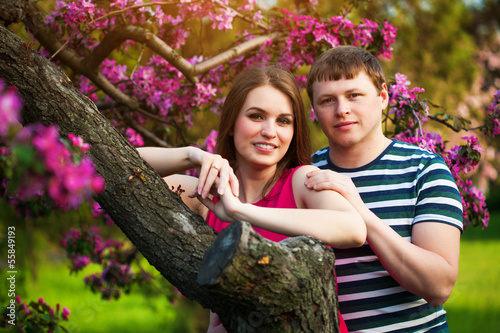 Photo: Happy loving couple are hugging blossoming apple orchard Happy loving couple are hugging blossoming apple orchard