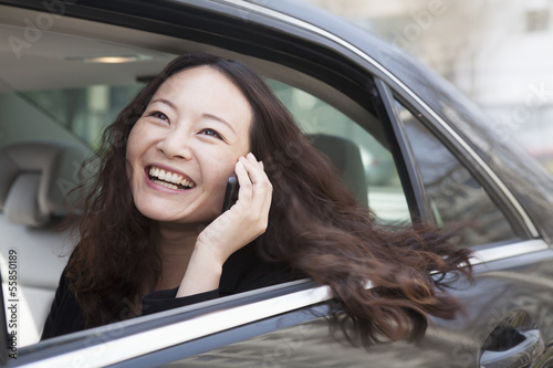 Photo: Young women in back seat of car using mobile phone. Young women in back seat of car using mobile phone.