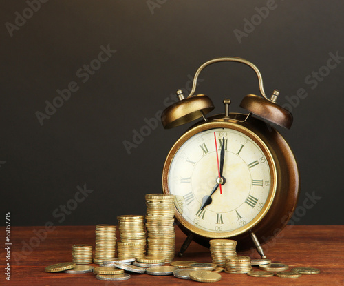 Photo: Antique clock and coins on wooden table on black background Antique clock and coins on wooden table on black background
