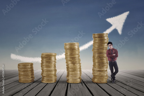 Photo: Confident businessman standing next to gold coins chart Confident businessman standing next to gold coins chart
