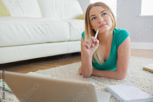 Photo: Thoughtful blonde lying on floor doing her assigment using lapto Thoughtful blonde lying on floor doing her assigment using lapto