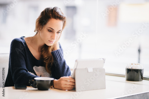 Photo: Young woman / student using tablet computer in cafe Young woman / student using tablet computer in cafe