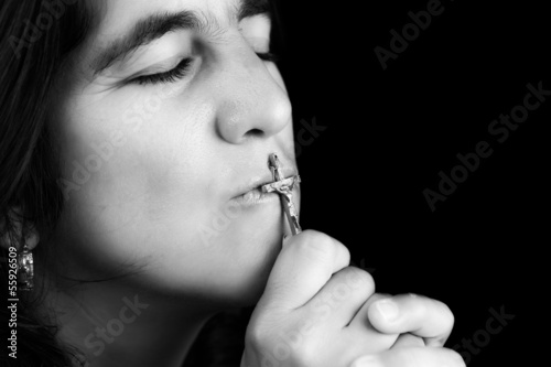 Photo: Hispanic woman kissing a small crucifix (isolated on black) Hispanic woman kissing a small crucifix (isolated on black)